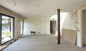 Wnętrze w budowie, widoczne nierówności i plamy na ścianach wskazują na grubość tynku gipsowego.