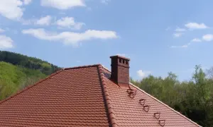 Solidna cegła klinkierowa na komin, dumnie wznosząca się nad czerwonym dachem.