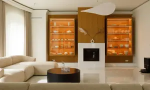 Nowoczesny salon z kominkiem, przeszklonymi witrynami z zastawą i beżową sofą.