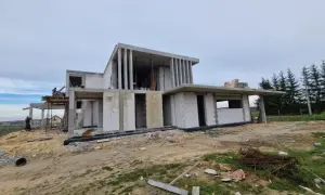 Budowa nowoczesnego domu z betonu i białych pustaków, w tle las.