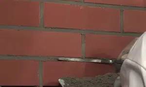 Pracownik nakłada fugę do klinkieru na ceglaną ścianę za pomocą kielni.