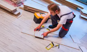 Fachowiec układa panele podłogowe, zastanawiając się, ile kosztuje położenie paneli. Wokół narzędzia i materiały.