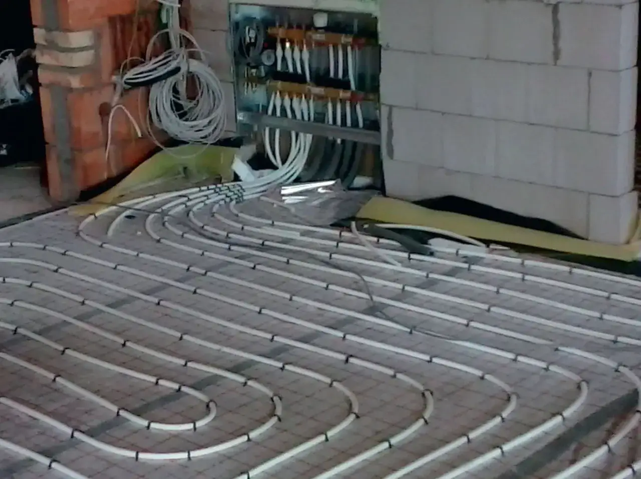 Instalacja ogrzewania podłogowego. Zastanawiasz się, ile kosztuje ogrzewanie podłogowe? Widoczny system rurek i rozdzielacz to kluczowe elementy.