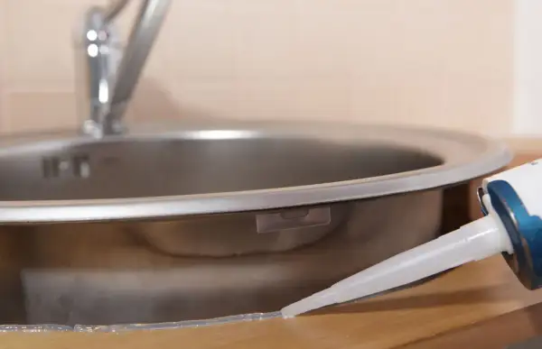 Aplikacja silikonu wokół zlewu. Zastanawiasz się, jak długo schnie silikon? Czas schnięcia zależy od wilgotności i temperatury.
