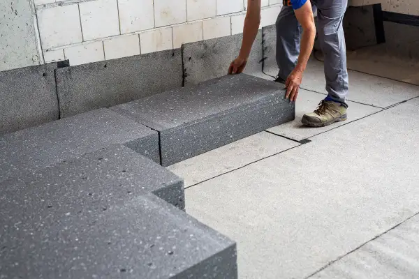 Układanie grubego styropianu pod wylewkę na budowie. Ręce pracownika precyzyjnie dopasowują płyty izolacyjne.