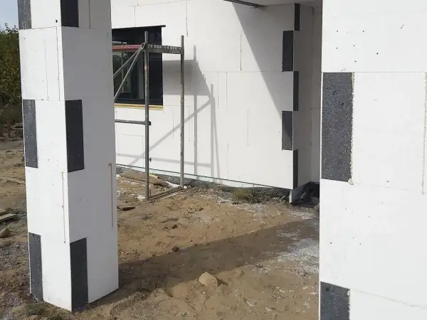 Budowa domu z bloczków styropianowych. Zastanawiasz się, czym przykleić styropian do blachy? Tutaj widzisz fragmenty ścian i słupa z białego styropianu z czarnymi wstawkami.
